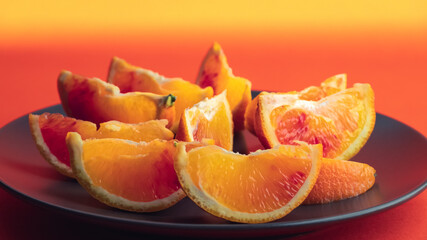 Obraz na płótnie Canvas Colorful fruit background. slices of red orange are on dark dish on bright orange background. Fresh citrus fruit rich of vitamins, healthy nutrition. Orange color
