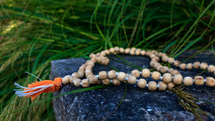 Close up of wooden prayer beads on stone with green grass outdoor. Zen mantra meditation and...