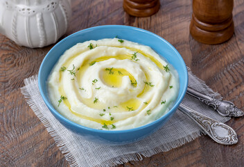 Creamy mashed cauliflower with melted butter and fresh herbs in a bowl on wooden rustic table. 