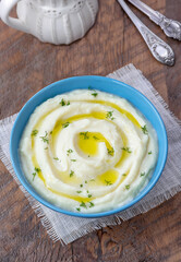 Smooth, fluffy cauliflower mashed potatoes with melted butter and fresh dill in a bowl on wooden table. 