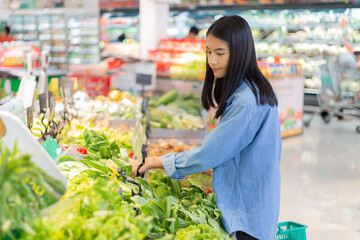 Young woman looking at vegetables at grocery store. female shopping in supermarket. Customer buying vegetables at the market.