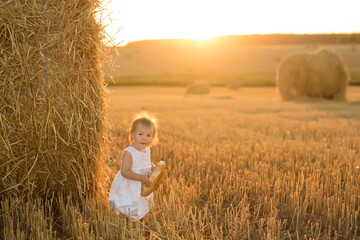 A little girl in a field next to a haystack. A girl with a funny hairstyle looks at me with her mouth open in surprise. A child holds gluten-free bread in his hands.