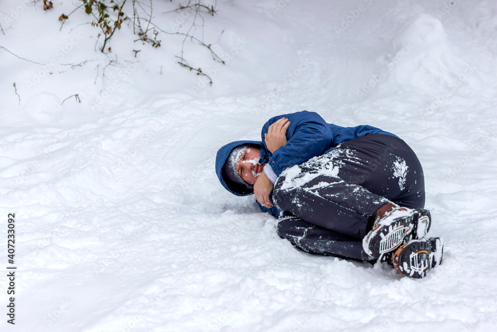 Wall mural photo of a frozen young man in blue jacket lying on the winter forest, covered snow. man mountaineer