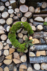 Close up shot of a country style christmas wreath made with moss and decorated with a pomegranate, hanging from a wall of neatly stacked firewood. Country house and living.