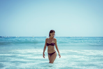 Beautiful young woman in bikini on vacation swimming in sea and enjoying in sand beach. Happy female enjoying summer time holiday on beach.