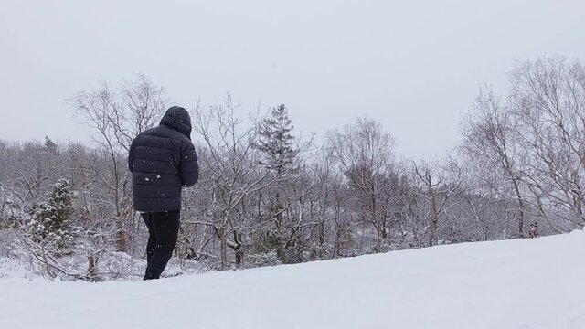 View of snow falling and a man trying to throw a snowball at a tree but misses. Slow motion video.
