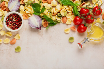 Raw orecchiette with parmesan cheese and tomatoes, basil, garlic and oil on light background with pepper on light brown background. Traditional ingredients for preparation of Italian pasta. Top view.