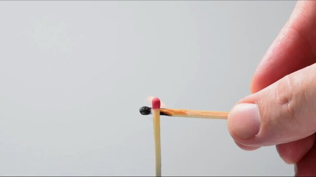 Man lighting a matchstick in an upright position on a light gray background.