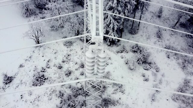 A shot from a drone, a frosted electric pole in a mountain scenery. Dangerously frozen transformer, harsh winter, low temperature.