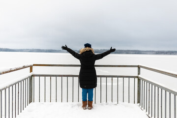 Woman spread her arms out near frozen lake in the distance the forest.