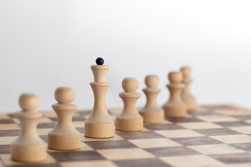 Chess queen among a row of pawns on a wooden chessboard