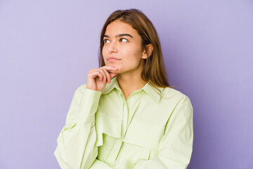 Young skinny caucasian girl teenager on purple background looking sideways with doubtful and skeptical expression.