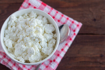 Homemade cottage cheese in a white bowl on a wooden background.