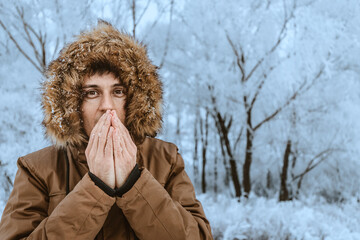 A man freezes in the cold in the forest and tries to wipe his hands with his breath. The concept of frostbite of the extremities and hypothermia of the body