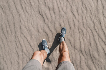 A hiker or jogger photographed his feet in shorts and running shoes against the background of sand