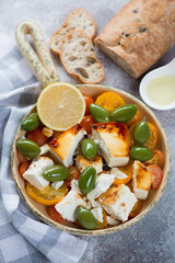 Chunks of feta cheese baked with tomatoes and green olives, vertical shot on a beige stone surface