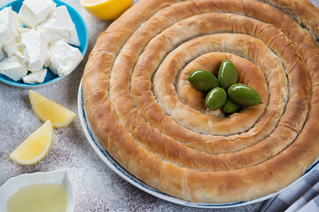 Greek spanakopita or spiral pie made of filo dough and stuffed with spinach and feta, studio shot over beige stone surface
