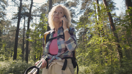 Plakat Senior woman backpacker talking on smartphone on trip in forest