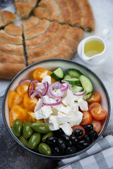 Bowl of greek salad and sliced spanakopita spiral pie in the background, vertical shot