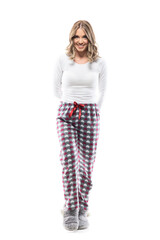 Friendly happy young woman in pajamas walking hiding gift behind back looking at camera. Full length portrait on white background.