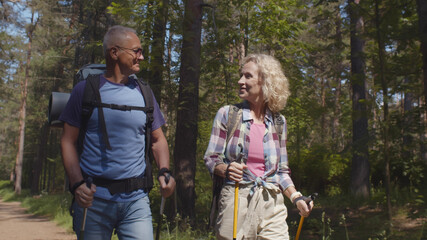 Cheerful senior caucasian couple hiking in park with backpacks, enjoying adventure