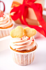 Valentines cupcakes cream cheese frosting decorated with heart shaped cookies and gift box on the background.