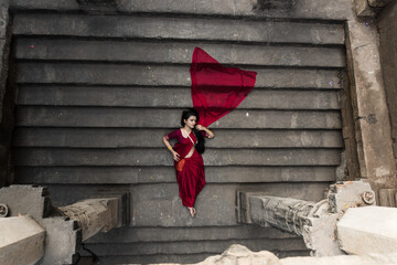 Portrait of beautiful Indian girl in heritage stepwell wearing traditional Indian red saree, gold...