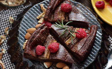 Chocolate vegan brownie cake with banana decorated with raspberry, walnut and rosemary, closeup, copy space, vegan eggfree desserts concept