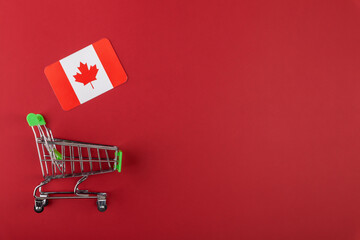 Mini empty supermarket shopping grocery cart, Canada flag on red background