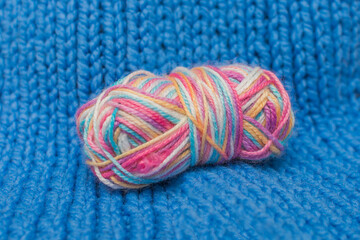 a multi-colored roll of thread lies on a blue knitted background. Close-up, horizontal photo....