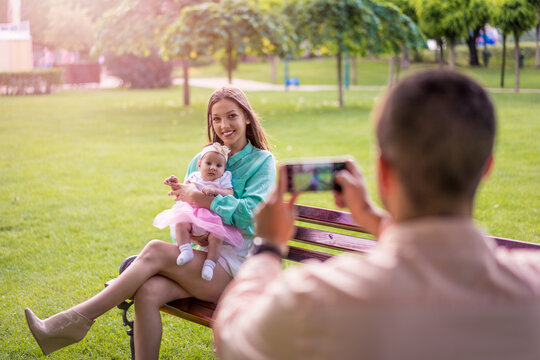 Beautiful young happy couple with baby in park outdoors. Love, parenthood, family, season and people concept - smiling couple. Parents play with their baby, father taking a photo