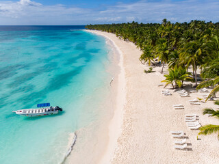 Aerial drone view of the paradise beach with palm trees, boats, sun beds, coral reef and blue water of Caribbean Sea, Saona island, Dominican Republic