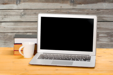 Fototapeta premium Laptop with blank screen, cup of coffee and books or notebooks on a wooden table. mockup for your text