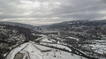 Aerial view of a snow-covered city park. Water intake on the Sochi river in winter. Beautiful view of the mountain peaks in the city.