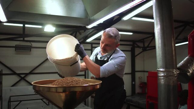 Man pouring coffee beans into the roaster machine indoors. 4k. Pedestal shot