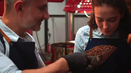 Couple of baristas in uniform checking the quality of roasted coffee beans standing near the roaster machine. Close up view. 4k