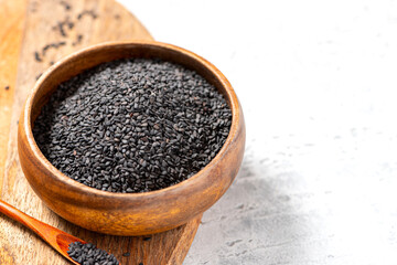 Black sesame seeds in a wooden bowl on a gray background close-up. Copy space for text.