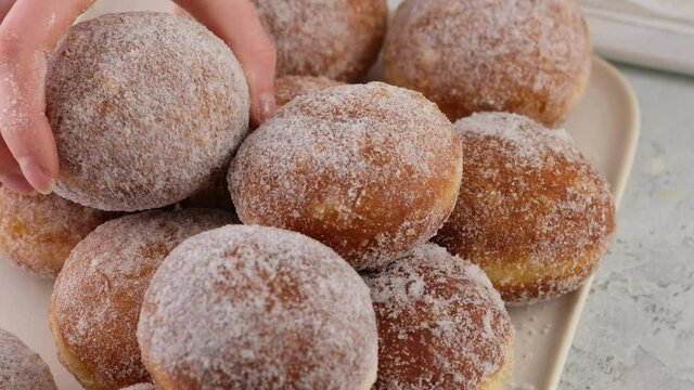 Close-up Berliners. Female hands lay donuts on a rectangular plate on a white background. Delicious sweet donuts. Making donuts with jam.