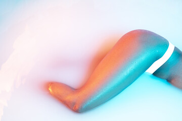 Flexible. Close up female body in the milk bath with soft white glowing in neon light. Copyspace for advertising. Modern neoned colors, foam. Beauty, fashion, style, bodycare concept. Attractive.