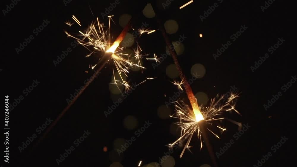 Poster two sparklers burning in the darkness with bokeh at background in 4x slow motion