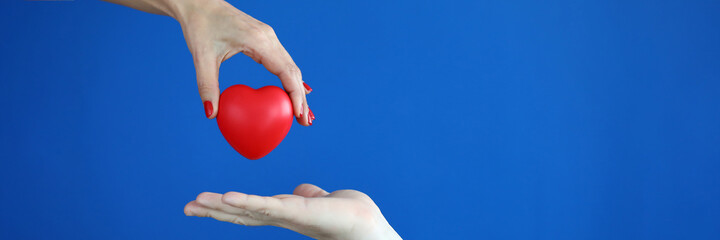 Hands with manicure pass the red heart to other hands. Healthy organ transplantation