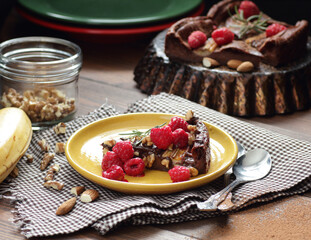 Chocolate vegan brownie cake with banana decorated with raspberry, walnut and rosemary, closeup, copy space, vegan eggfree desserts concept