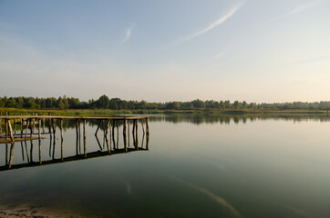 Old piers are reflected in the water of the lake. The sky is reflected in the water surface. Morning landscape. Peace and quiet in the countryside.