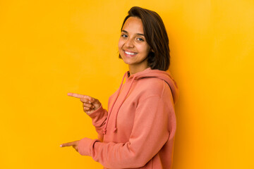 Young hispanic woman isolated on yellow excited pointing with forefingers away.