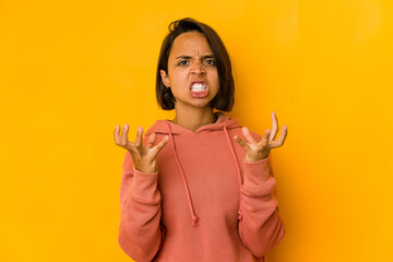 Young hispanic woman isolated on yellow upset screaming with tense hands.