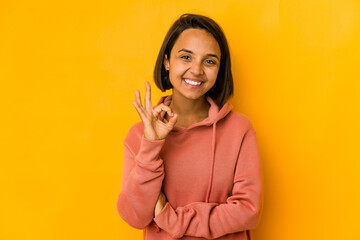 Young hispanic woman isolated on yellow cheerful and confident showing ok gesture.