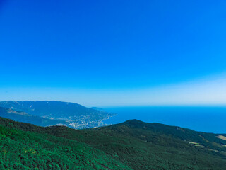 Beautiful landscape of green forest hills on the background of blue sea and clear sky.