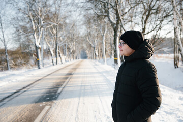 Young man in black in winter admires snowy landscape, standing by road.