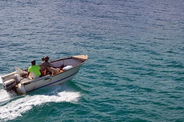 Two fishermen returning from a morning at sea in a fishing skiff powered by a single outboard...