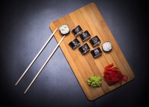 wooden board with Japanese fish rolls, ginger and wasabi and chopsticks on black background